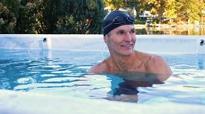 man in swim cap smiling submersed in swim spa water