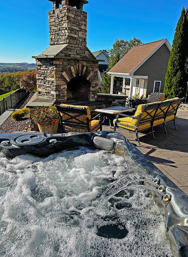 pdc spas hot tub on paver patio with large stone fireplace and patio seating