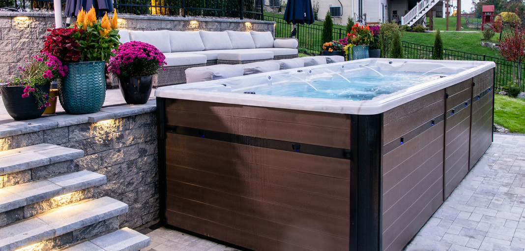 pdc swim spa installed on brick patio with brown cabinet and patio furniture