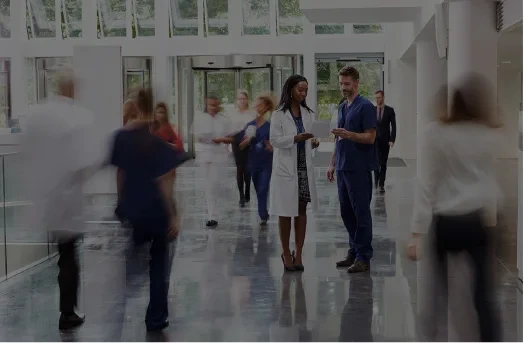 Doctors and medical staff walk and talk in a bright hospital corridor with large windows.
