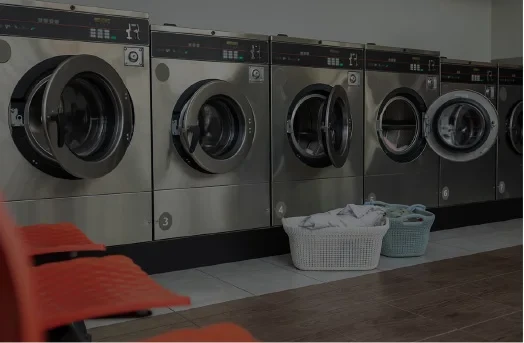 Front-load washing machines with open doors and laundry baskets filled with clothes in front.