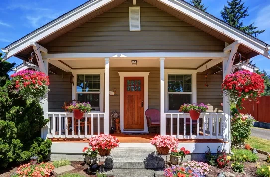 A small house with a wooden porch, flowers, and hanging plants in front of the entrance.