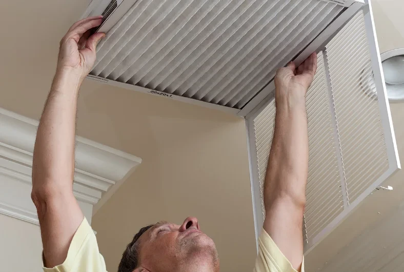 A person changes an air filter in a ceiling vent at home.