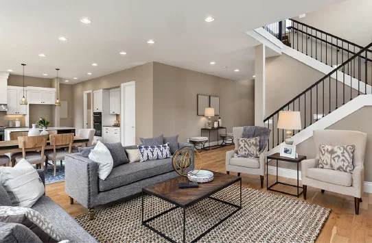 Modern living room with gray sofas, armchairs, a coffee table, and a view of a staircase.