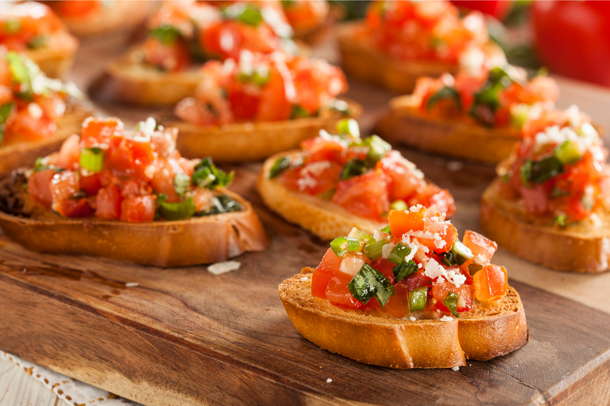 Crostini topped with diced tomatoes, herbs, and cheese on a wooden serving board.