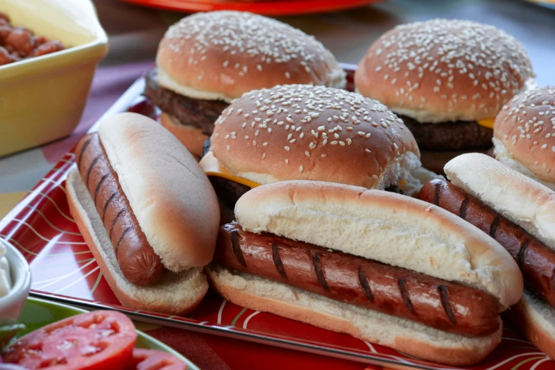 Grilled hot dogs and cheeseburgers in buns arranged on a red platter at a picnic.