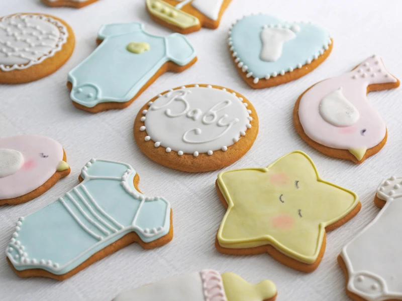 Assorted baby-themed decorated cookies, including onesies, a star, a bird, and a Baby cookie.