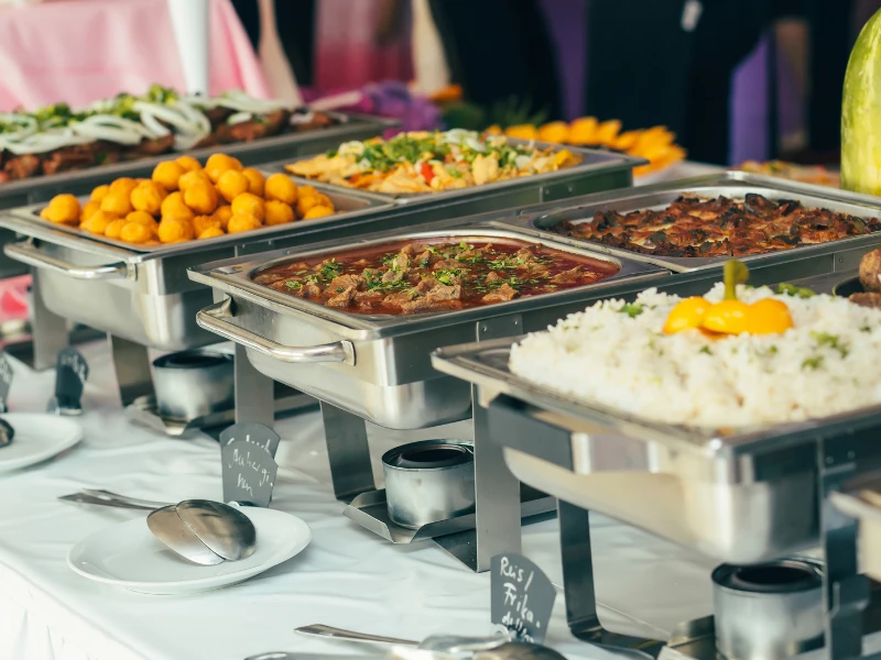 A buffet table with chafing dishes filled with rice, meat, vegetables, and fried appetizers.