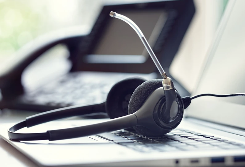 A headset rests on a laptop keyboard, with an office phone blurred in the background.