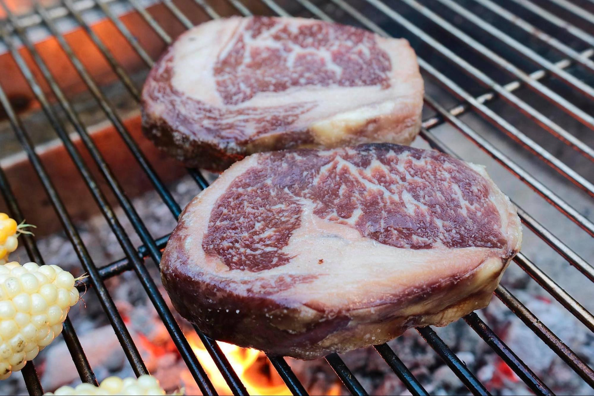 raw steaks on grill with corn