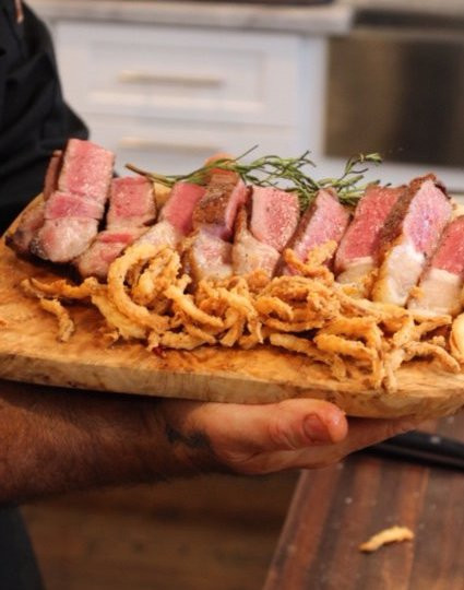 frizzled onions next to a sliced steak on a wood platter