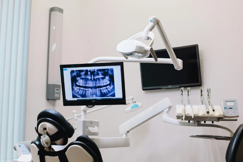 A dental office with a chair, x-ray on a monitor, and dental equipment nearby.