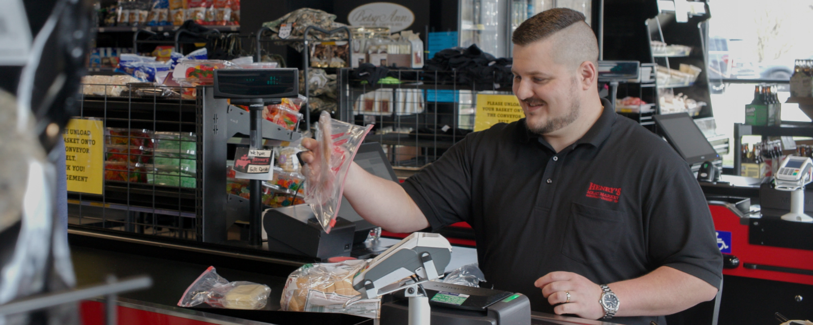 Smiling cashier scans groceries at the checkout counter in a store.