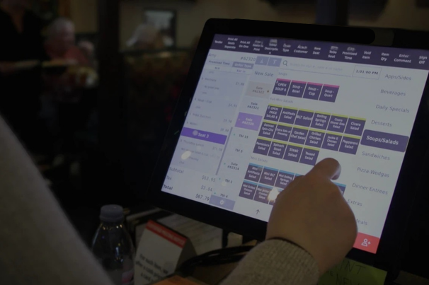 A person uses a touchscreen point-of-sale system in a dimly lit restaurant setting.
