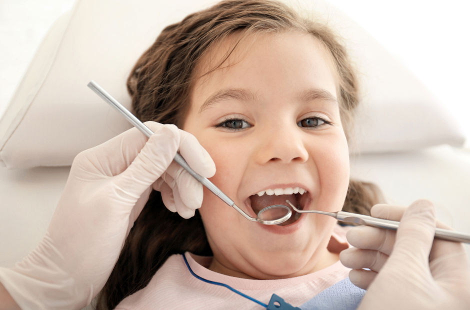 Smiling girl at the dentist having her teeth examined with dental tools.